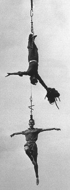 Escapologis Karl Bartoni at the end of his escape from a strait-jacket whilst hanging from a burning rope, with circus artist Marcia Spence hanging by her hair from him. Blackpool 1986